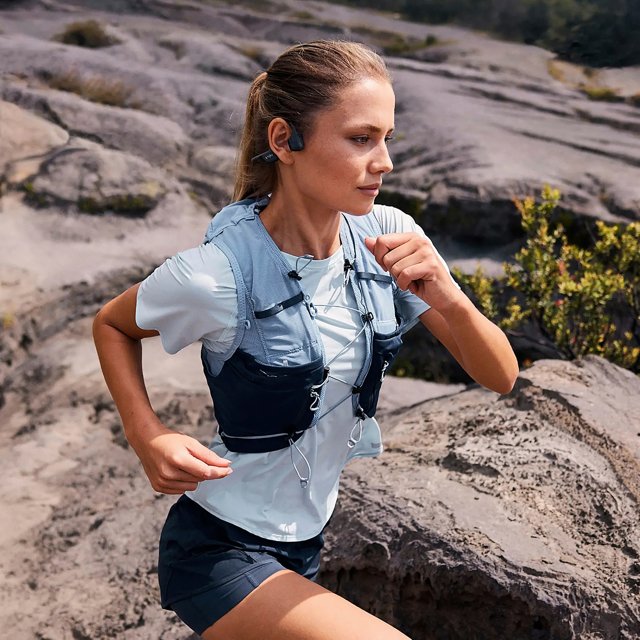 Vrouw hardloopt over een rotsachtig pad met de zwarte Shokz OpenRun Pro 2 Mini Zwart hoofdtelefoon – lichtgewicht en veilig sporten – HearPlanet