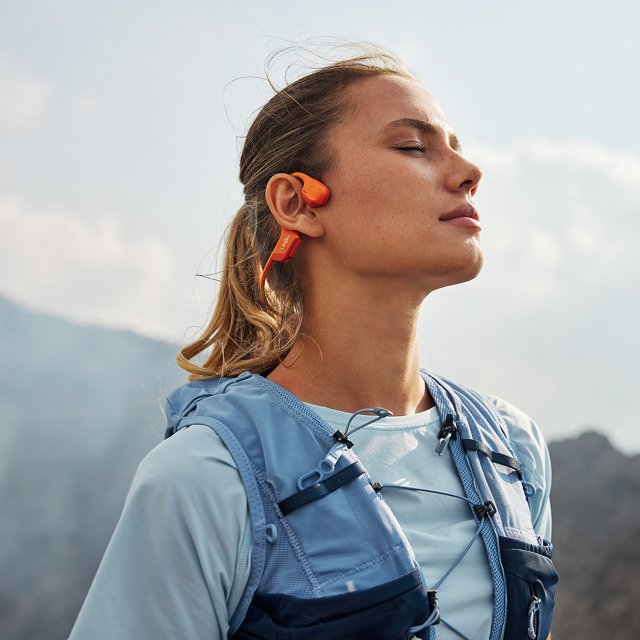 Vrouw geniet van muziek met de Shokz OpenRun Pro 2 oranje tijdens het hardlopen – bone conduction sportkoptelefoon – HearPlanet. Vrouw geniet van muziek met de Shokz OpenRun Pro 2 oranje tijdens het hardlopen – bone conduction sportkoptelefoon – HearPlanet.