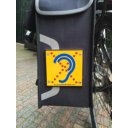 Limited Hearing reflecterend bordje gemonteerd op zijkant van fietstas met geel herkenningsteken Limited Hearing reflecterend bordje gemonteerd op zijkant van fietstas met geel herkenningsteken